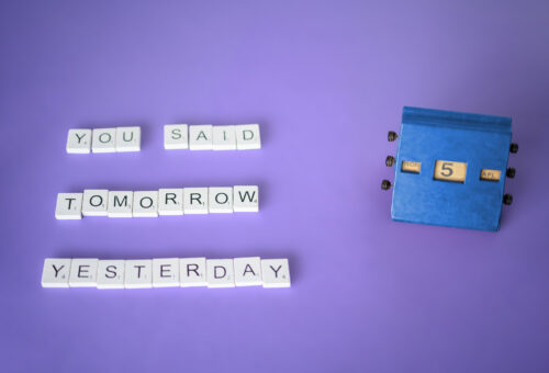 Letter tiles on a purole background spelling "you said tomorrow yesterday" next to a desk calendar