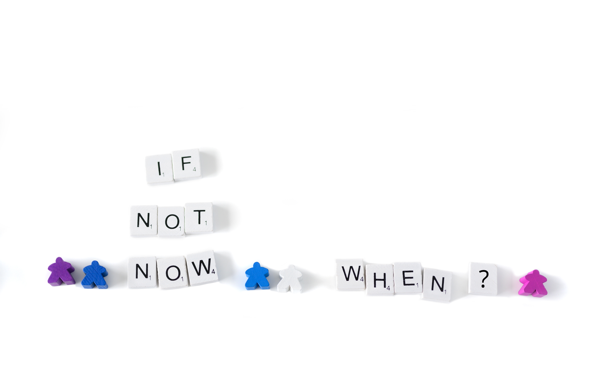Scrabble tiles spelling out “If not now, when?” with small coloured game pieces representing people standing around the words.
